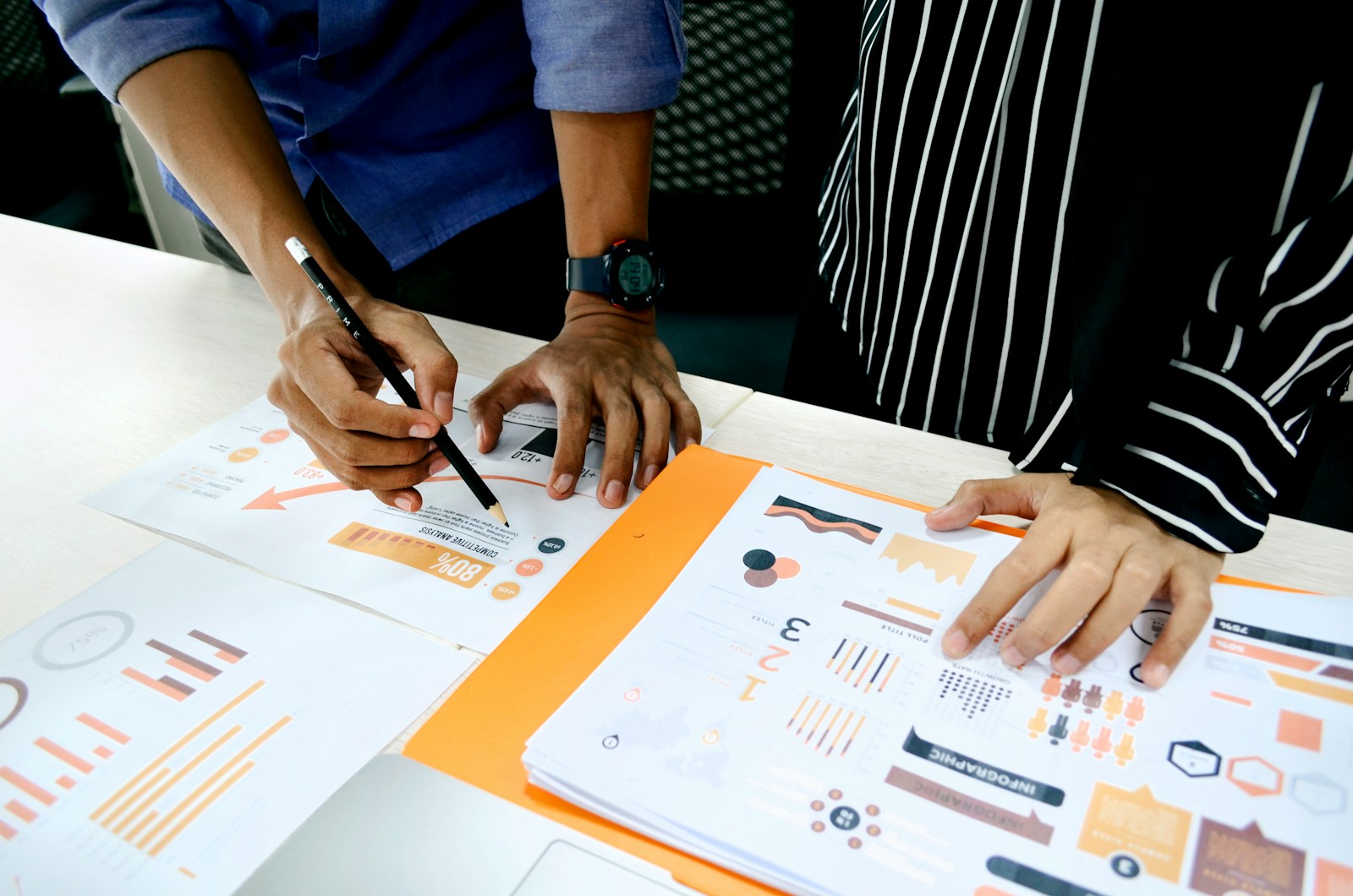 Two people collaborate on data analysis, focusing on graphs and charts displayed on papers. A pencil is used for annotations during the discussion.